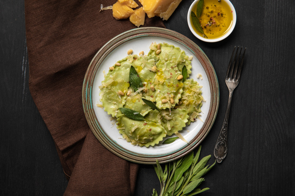 top view of green ravioli served in vintage plate near silver fork and napkin at black wooden table - 写真・画像