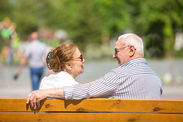 Senior couple wearing sunlglasses relaxing sitting on a bench in city park - Fotó, kép