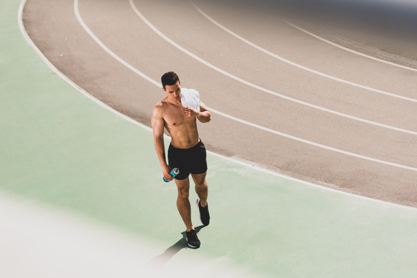 pełny widok długości mieszanej rasy sportowca trzymający ręcznik i butelkę sportową na stadionie - Zdjęcie, obraz