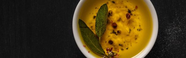 top view of aromatic oil in bowl with spices and herbs on black table, panoramic shot - Photo, Image