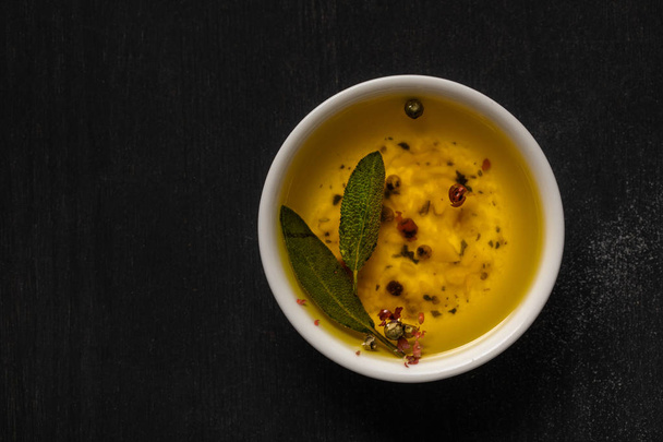 top view of aromatic oil in bowl with spices and herbs on black table - Foto, Imagem