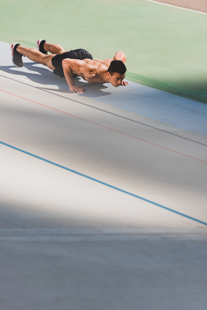 shirtless mixed race sportsman doing push ups at stadium - Φωτογραφία, εικόνα