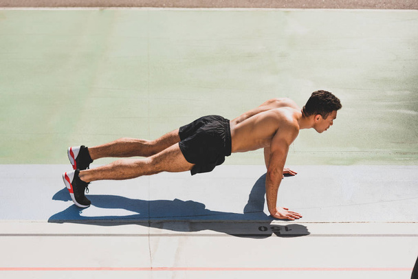 mixed race sportsman standing in plank at stadium - Foto, immagini
