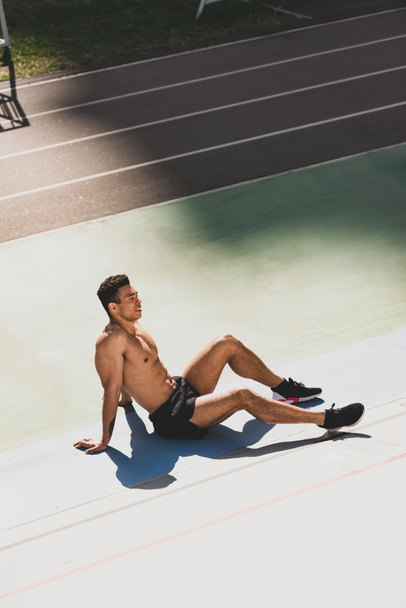 tired handsome mixed race sportsman sitting at stadium - Photo, Image