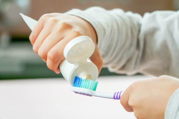 Dziecko stosuje szczoteczkę do zębów i pastę do zębów na niewyraźne tło - Zdjęcie, obraz