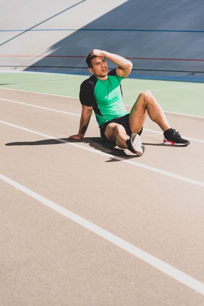 fáradt vegyes verseny sportoló ül a stadionban, és megható fejét - Fotó, kép