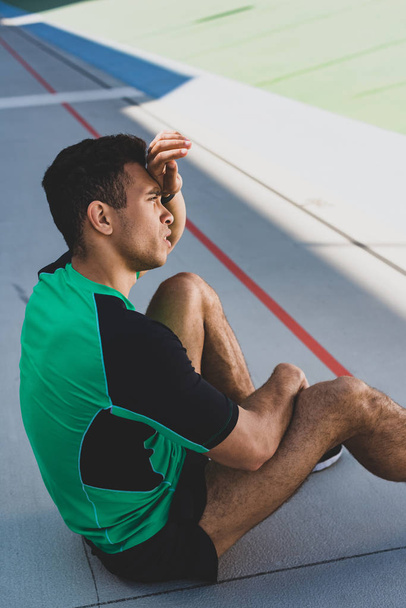 tired handsome mixed race sportsman sitting at stadium - Photo, Image