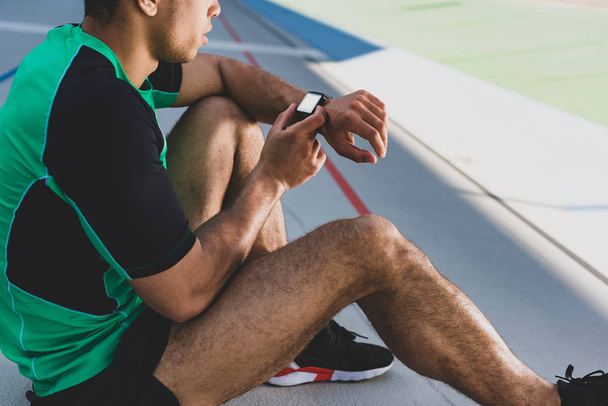 περικομμένη θέα του αθλητή με το έξυπνο ρολόι στο τρέξιμο Track  - Φωτογραφία, εικόνα