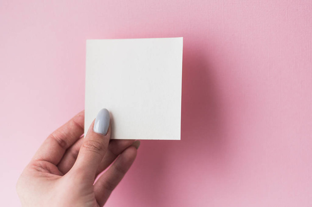 Minimaalinen vaalea koostumus, jossa tytön käsi pitää korttia vaaleanpunaisella pastellitaustalla. Tasainen, ylhäältä
. - Valokuva, kuva