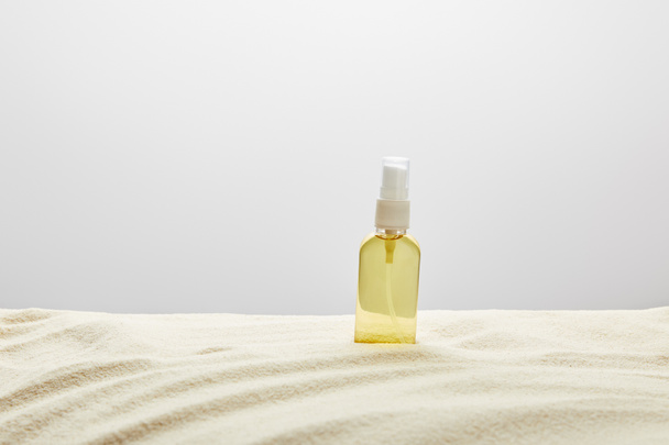 suntan oil in transparent yellow spray bottle in sand on grey background - Foto, afbeelding