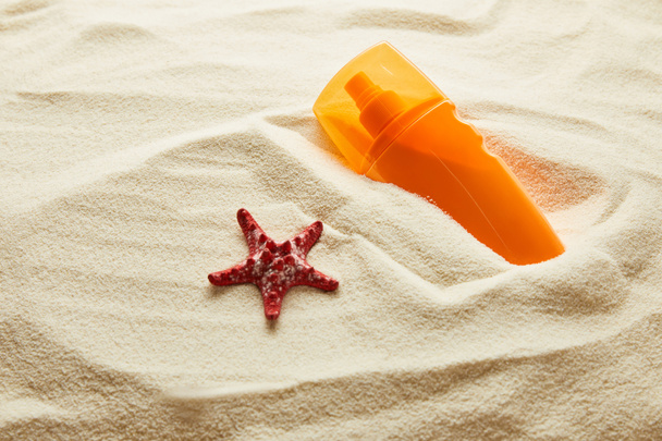 dokulu kum turuncu şişede kırmızı denizyıldızı ve güneş kremi - Fotoğraf, Görsel