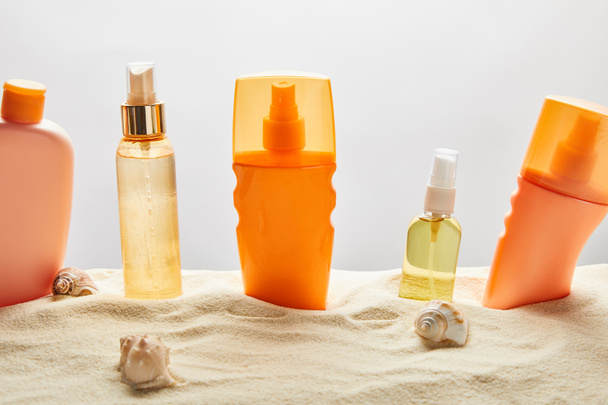 灰色の背景に貝殻を持つ砂の上のボトルの様々な日焼け止め製品 - 写真・画像