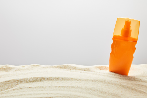 Αντηλιακή κρέμα σε πορτοκαλί φιάλη ψεκασμού στην άμμο σε γκρίζο φόντο - Φωτογραφία, εικόνα