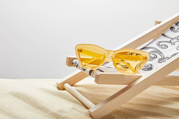 yellow sunglasses and deck chair on sand on grey background - Photo, Image
