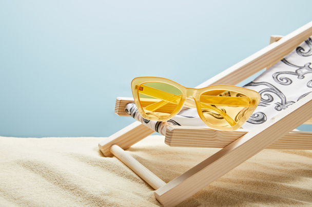lunettes de soleil jaunes et chaise longue sur sable sur fond bleu
 - Photo, image