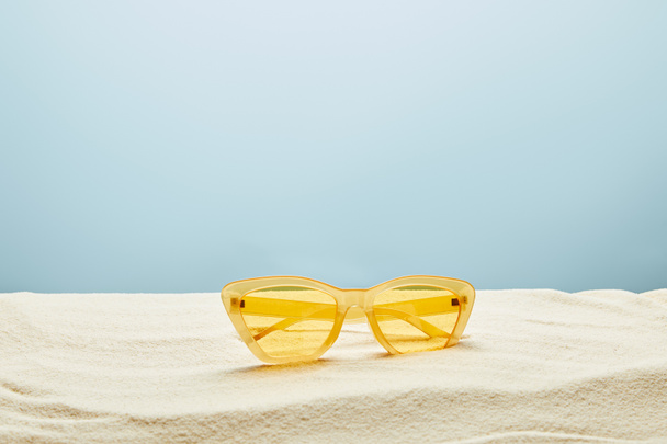yellow stylish sunglasses on sand on blue background - Photo, Image