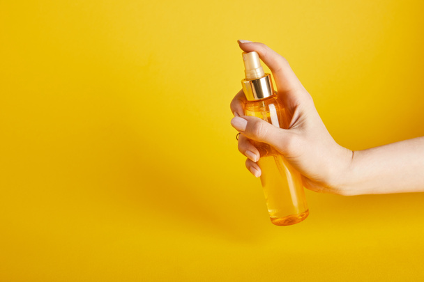cropped view of woman holding suntan oil in spray bottle on yellow background - Photo, Image