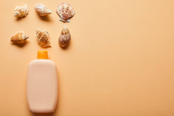 flat lay with sunscreen lotion in bottle near seashells on beige background - Photo, Image