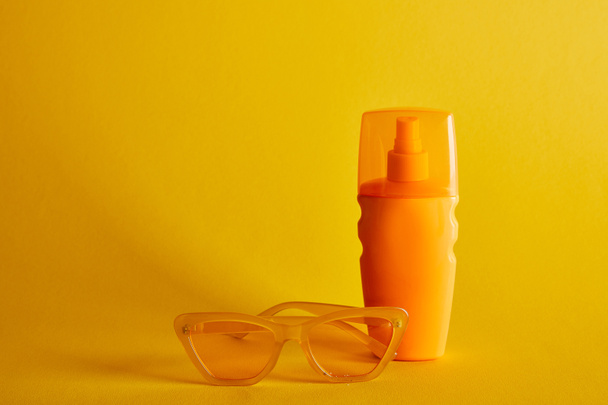 sunscreen in orange bottle near sunglasses on dark yellow background - 写真・画像