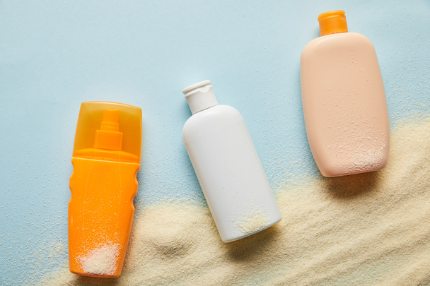 top view of sunscreen products in bottles on blue background with sand - Photo, Image