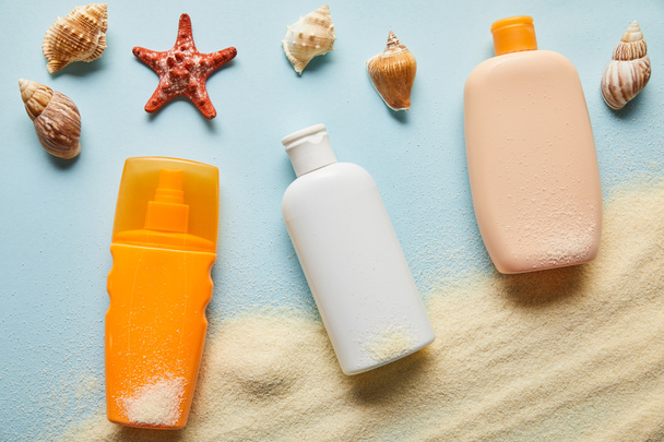 top view of sunscreen products in bottles on blue background with sand, starfish and seashells - Photo, Image