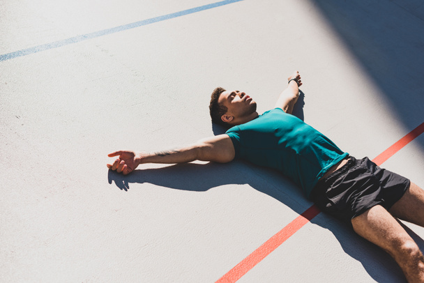 mixed race sportsman laying on running track and spread arms in sunlight - Photo, Image