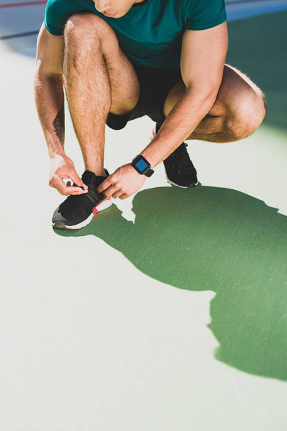 ostříhané zobrazení sportovce rozvazující tenisky na stadionu - Fotografie, Obrázek
