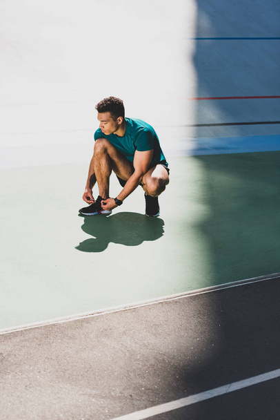 mixed race sportsman lacing up sneakers at stadium - 写真・画像