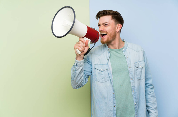 Redhead muž na barevném pozadí křičící přes megafon - Fotografie, Obrázek