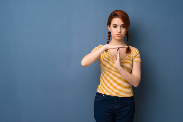 Fiatal vörös hajú nő a kék háttér így stop gesztus a kezét, hogy hagyja abba a cselekmény - Fotó, kép