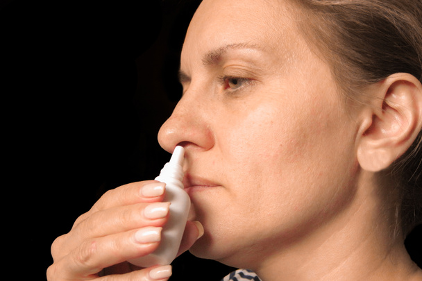 Nahaufnahme einer Frau mittleren Alters, die Nasentropfen in die Nase tropft - Foto, Bild