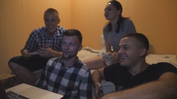 Grupa ludzi oglądając film komediowy lub śmieszne wideo mediów społecznościowych na laptopie w domu. Happy Man jedzenia przekąsek patrząc online TV show na komputerze. Młoda dziewczyna głaszcząc kota siedzącego w łóżku - Materiał filmowy, wideo