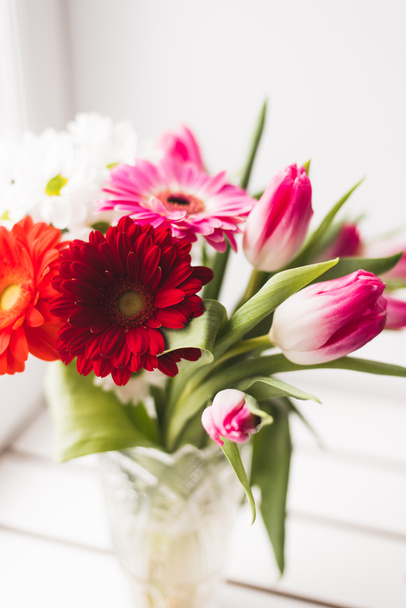 kukkakimpun gerberat, tulppaanit ja krysanteemit. kimppu kirkkaan tuoreita kukkia maljakko kevyellä taustalla
 - Valokuva, kuva