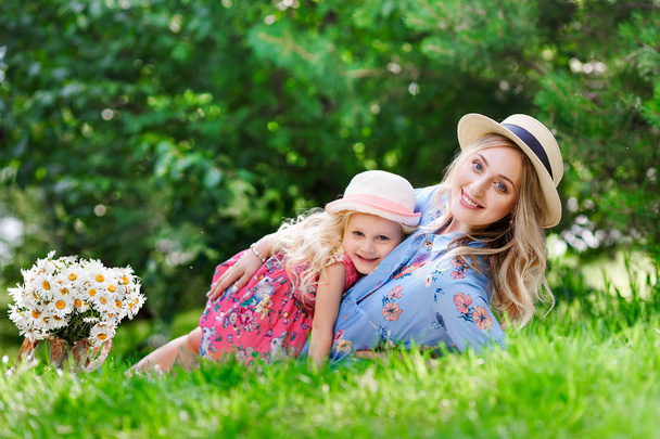 Portraitof a beautiful pregnant mother in a straw hat lie near to her little daughter in a park on a sunny summer day. The concept of happy family relationships. - Foto, Imagen