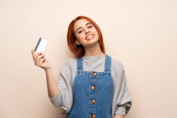 Młoda ruda kobieta na odosobnionym tle z kartą kredytową i myśleniem - Zdjęcie, obraz