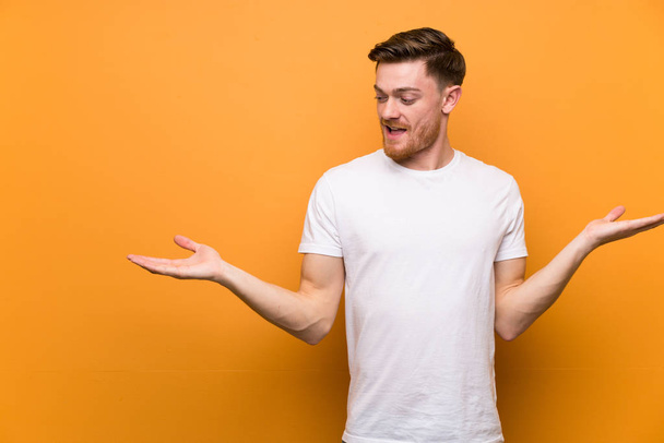 Redhead man over brown wall holding copyspace with two hands - Photo, Image