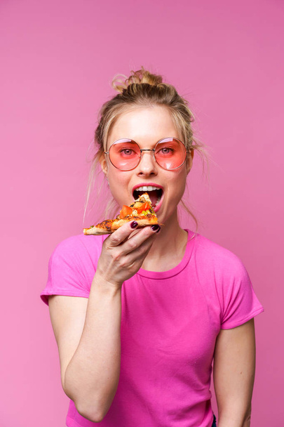Image of blonde in pink t-shirt with piece of pizza in her hands - Fotó, kép