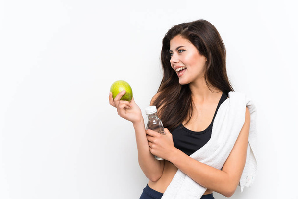 Teenager Sportmädchen über isolierten weißen Hintergrund mit einem Apfel und einer Flasche Wasser - Foto, Bild