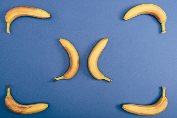 Вид сверху на вкусные, спелые и желтые бананы на синем фоне
 - Фото, изображение