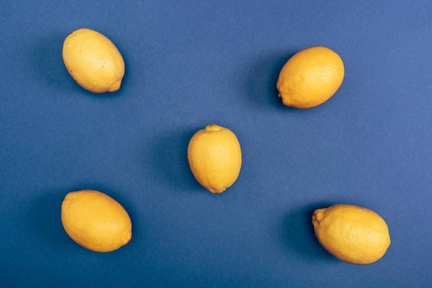 Вид сверху свежих ярко-желтых лимонов на синем фоне
 - Фото, изображение