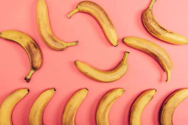 Top view of delicious and tasty yellow bananas on coral background - 写真・画像