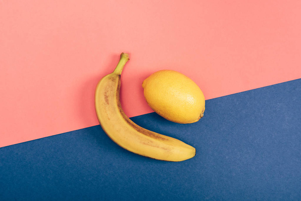 Top view of yellow banana and juicy lemon on multicolored coral and blue background - Fotografie, Obrázek