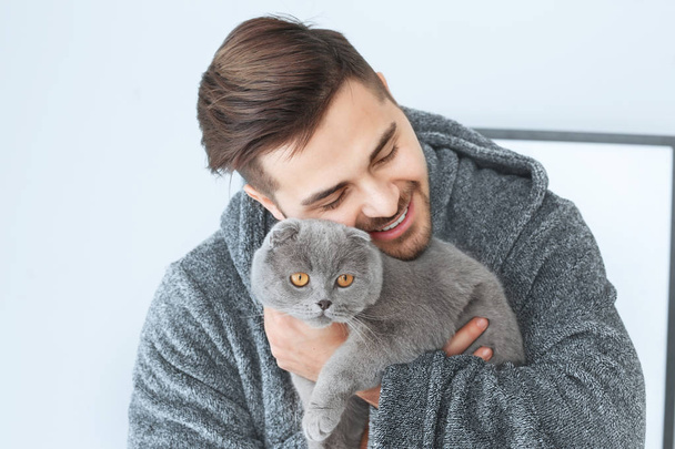 Young man with cute funny cat at home - Фото, изображение