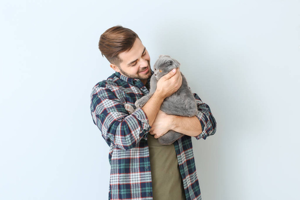 Young man with cute funny cat on light background - Zdjęcie, obraz