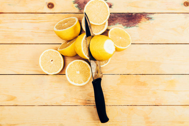 Top view of fresh and yellow cut lemons with knife on wooden table background - Photo, image