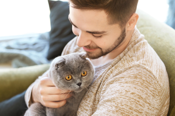Young man with cute funny cat at home - Foto, Imagen