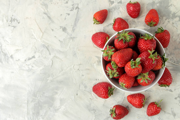Ripe, delicious strawberries. Red strawberry in a ceramic bowl on a light concrete table. top view - Foto, imagen