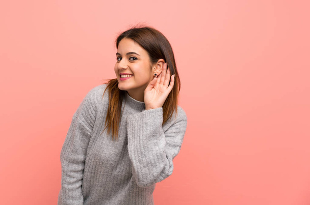 Jeune femme sur le mur rose écoutant quelque chose en mettant la main sur l'oreille
 - Photo, image