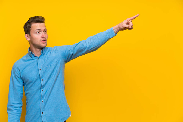 Blonde man over isolated yellow wall pointing away - Photo, Image