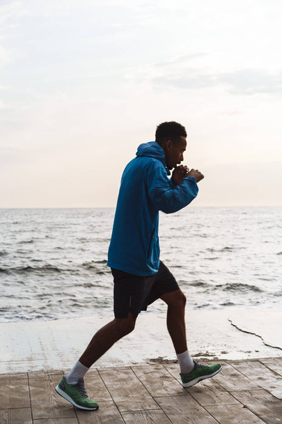 Strong handsome young african sports man boxer outdoors at the beach sea walking make boxing exercises. - Foto, imagen